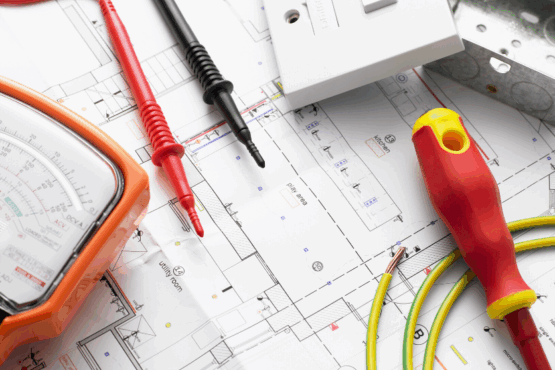 Electrical tools and circuit tester laid out on top of building plans for system design and installation