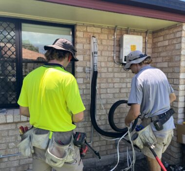 Two air conditioning technicians preparing conduit and piping for a residential split-system AC installation