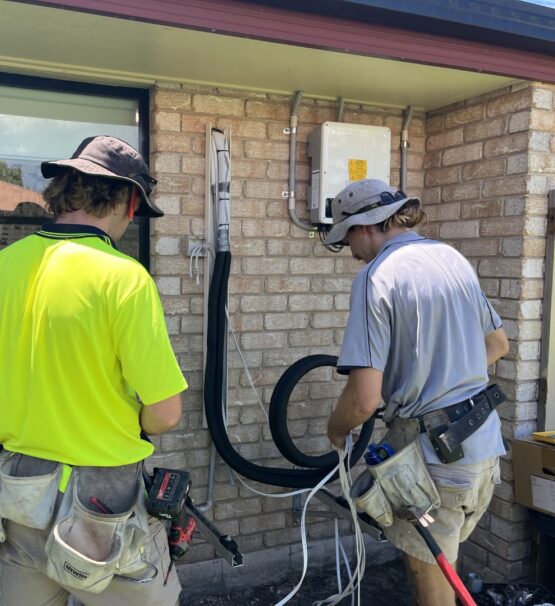 Two air conditioning technicians preparing conduit and piping for a residential split-system AC installation
