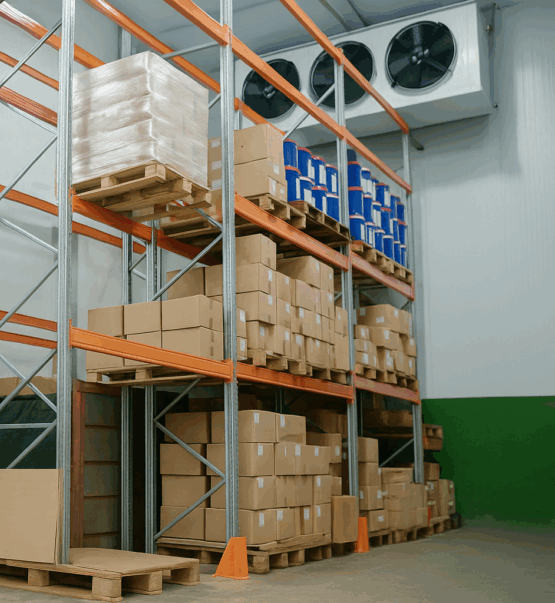 Warehouse interior showing tall racking shelves stocked with boxes and paint buckets, featuring wall-mounted industrial cooling fans for cold storage.