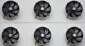 Six industrial air conditioning condenser fans mounted on an exterior facility wall for large-scale cooling