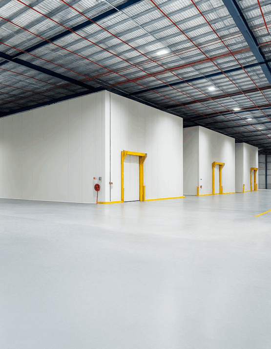 Wide-angle view of an industrial warehouse with insulated cold storage rooms, yellow-framed access doors, and a high ceiling with steel beams and lighting.