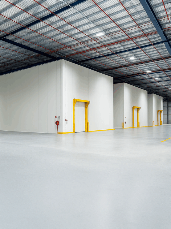 Wide-angle view of an industrial warehouse with insulated cold storage rooms, yellow-framed access doors, and a high ceiling with steel beams and lighting.