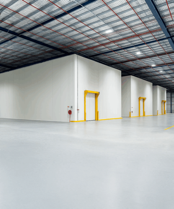 Wide-angle view of an industrial warehouse with insulated cold storage rooms, yellow-framed access doors, and a high ceiling with steel beams and lighting.