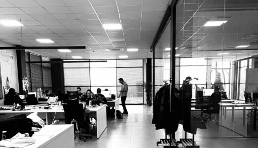 Modern open‑plan office with desks, overhead lighting and a glass‑walled meeting room.