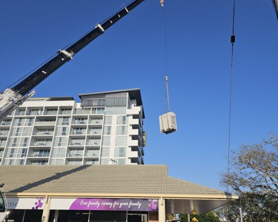 Crane lifting large electrical equipment onto a commercial building during a PowerControl Industries installation
