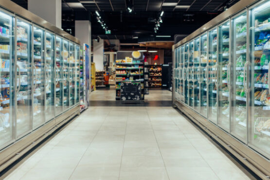 Supermarket aisle with glass‑door commercial refrigeration units stocked with chilled products