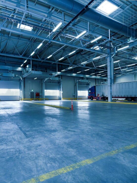 Interior of a large commercial warehouse with high-bay lighting, roller doors, and integrated ducting