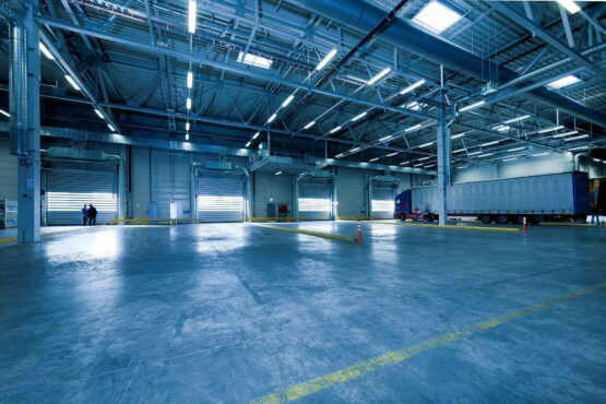 Interior of a large commercial warehouse with high-bay lighting, roller doors, and integrated ducting